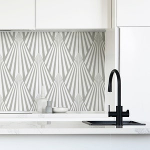 May include: A white kitchen with a grey and white geometric patterned backsplash. A black faucet is mounted above a black sink. A white countertop with a wooden stool is in the foreground. The text "THINK NOIR" is printed in black on the lower right corner of the image.