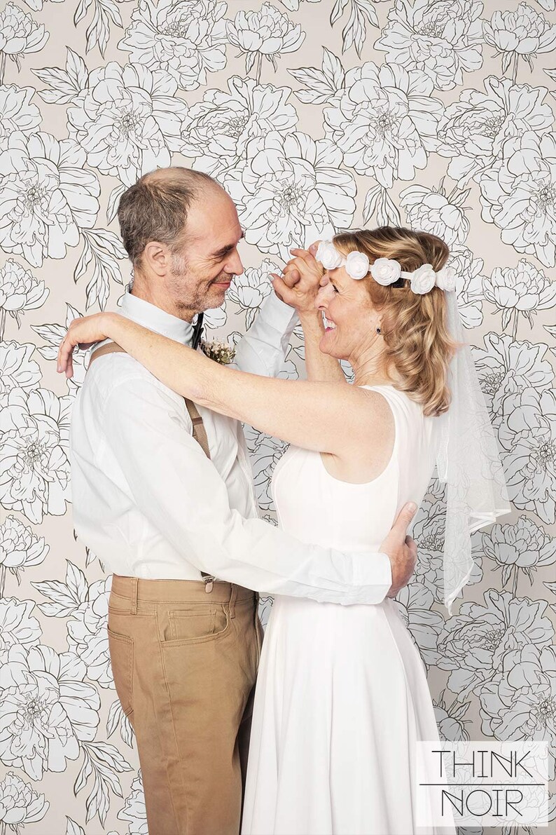 Newlyweds posing with a light peony pattern wallpaper in the background.