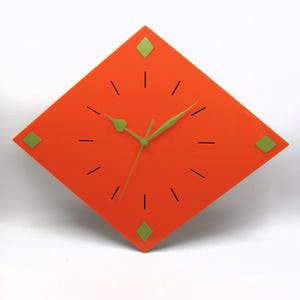 May include: A modern, orange, diamond-shaped wall clock with green accents. The clock features green hands and green diamond-shaped markers at the corners. Black lines mark the hours. A stylish, contemporary home decor item.