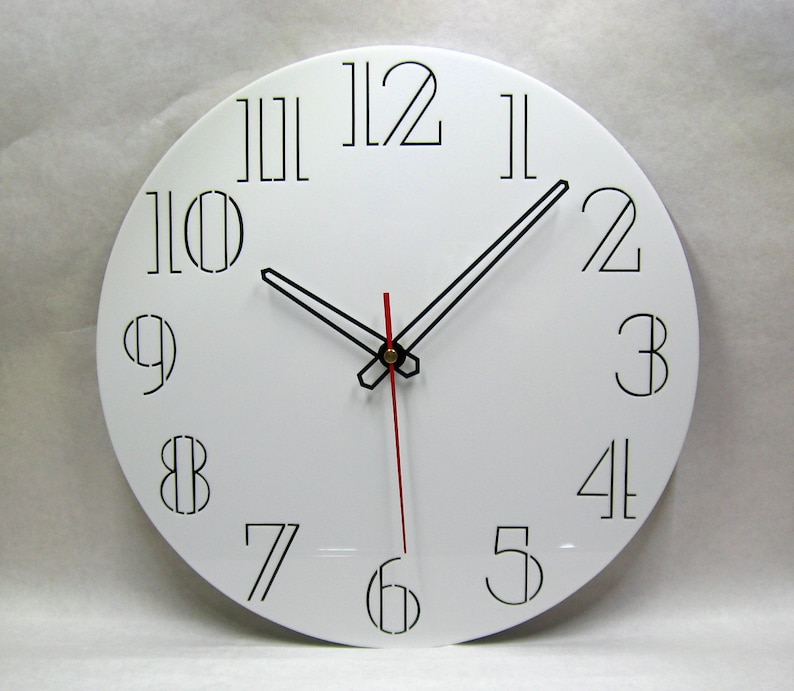 K&ouml;nnte beinhalten: Eine wei&szlig;e runde Uhr mit schwarzen r&ouml;mischen Ziffern als Stundenmarkierungen und schwarzen Zeigern. Der Minutenzeiger ist rot.