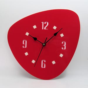 May include: A red, irregularly shaped wall clock with white numbers and black hands. The clock has a modern design.