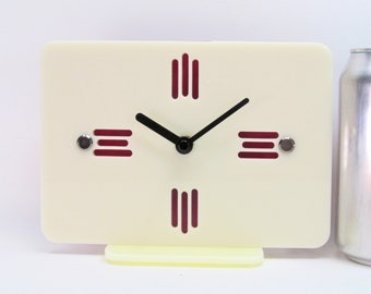 Könnte beinhalten: Eine weiße Uhr mit schwarzem Zifferblatt und roten Stundenmarkierungen. Die Uhr hat ein schlichtes Design und ist perfekt für ein modernes Zuhause.