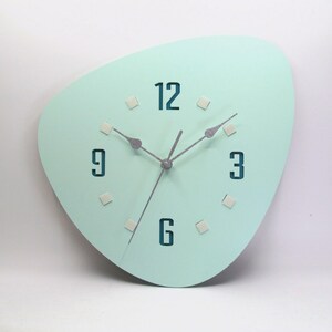 May include: A light blue, irregularly shaped wall clock with silver hands and black numbers. The numbers 12, 9, 3, and 6 are visible.