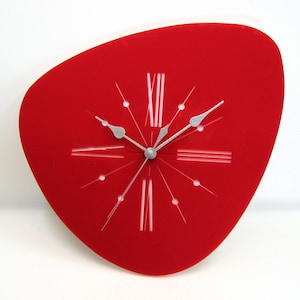May include: A red, abstract-shaped wall clock with silver hands and white Roman numeral markings.