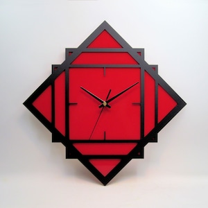 May include: A red clock with black hands and a black frame. The frame is made of overlapping squares, creating a geometric design.