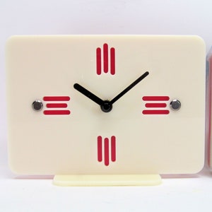 May include: A white clock with red hour markers and black hands. The clock has a simple design and is perfect for a modern home.