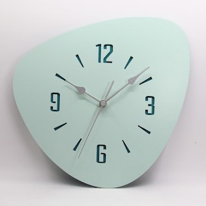 May include: A light green, irregularly shaped wall clock with silver hands and black numbers. The numbers 12, 3, 6, and 9 are visible.