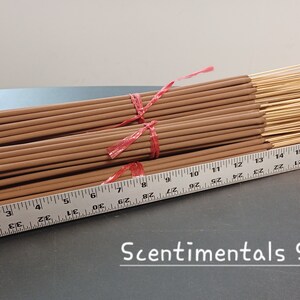 May include: Bundles of incense sticks, tied with red ribbon, are displayed next to a ruler. The incense sticks are a light brown color. The ruler shows measurements in inches. The text "Scentimentals Studio" is visible.