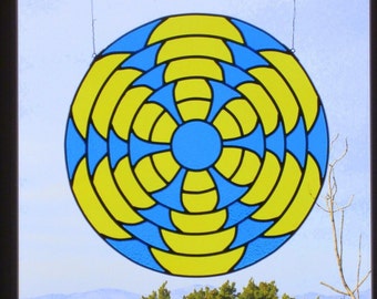 Puede incluir: Una ventana de vitrales con un diseño circular que presenta anillos concéntricos de color amarillo y azul. El centro del diseño es un círculo azul.