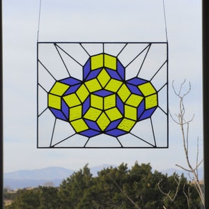 Könnte beinhalten: Ein Buntglasfenster mit einem geometrischen Muster aus gelben und blauen Glasscheiben. Das Muster ist ein komplexes Muster aus sich überlappenden Würfeln.