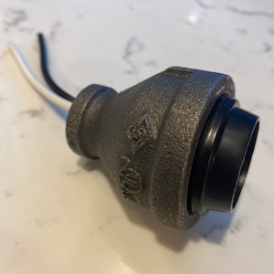 May include: A black and gray metal electrical outlet with two white wires attached. The outlet is designed to be used with a light fixture.