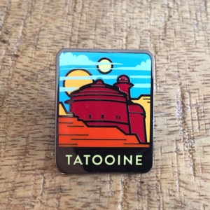 May include: A red and white enamel pin featuring a cartoon illustration of a building on a desert planet. The pin has the text "TATOOINE" at the bottom.