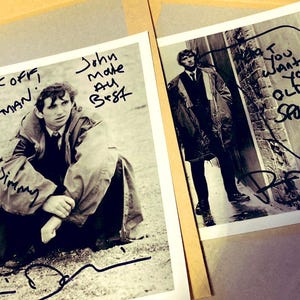 May include: Two black and white photographs featuring a man in a coat. One photo has the text "Fuck off, Mr. Postman" and "Jimmy" written on it. The other photo has the text "I want you old sponker". Both photos are signed.