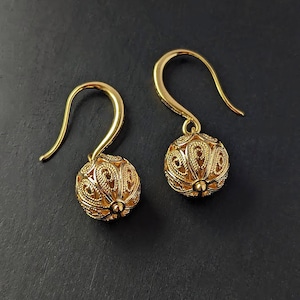 Puede incluir: Un par de pendientes de filigrana dorada con un diseño redondo calado. Los pendientes tienen un cierre de gancho simple.
