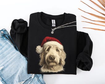 Può includere: Felpa nera girocollo con un'illustrazione dettagliata di un cane con un cappello di Babbo Natale. Il cane ha il pelo marrone chiaro e un'espressione concentrata. Una collana d'argento con un piccolo ciondolo è drappeggiata sulla felpa. La felpa è abbinata a jeans blu.