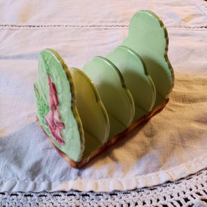 May include: A green ceramic bread knife holder with a floral design. The holder has four slots for bread knives.