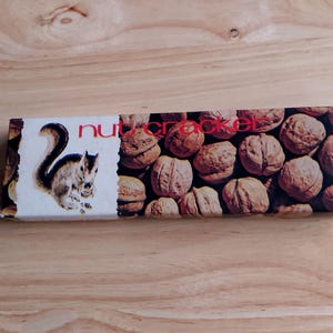 May include: A vintage nutcracker box featuring a squirrel illustration and the text "nut cracker" on the front. The box is filled with images of walnuts.