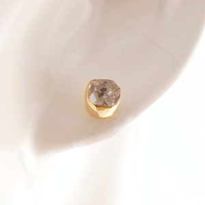 K&ouml;nnte beinhalten: Ein einzelner goldener Ohrring mit einem klaren, facettierten Edelstein.