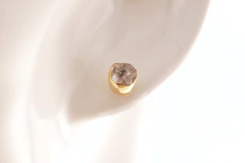 K&ouml;nnte beinhalten: Ein einzelner goldener Ohrring mit einem klaren, facettierten Edelstein.