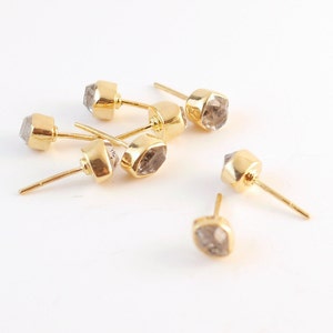K&ouml;nnte beinhalten: Sechs goldene Ohrstecker mit klaren, facettierten Steinen. Die Steine sind hellgrau und haben eine geometrische Form.