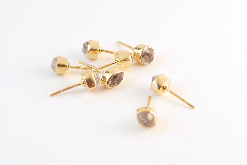 K&ouml;nnte beinhalten: Sechs goldene Ohrstecker mit klaren, facettierten Steinen. Die Steine sind hellgrau und haben eine geometrische Form.
