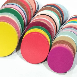 May include: A collection of colorful, circular leather pieces in various shades, including yellow, red, green, and pink. The leather circles are stacked, showcasing a variety of textures and hues. These leather pieces are suitable for crafting projects.