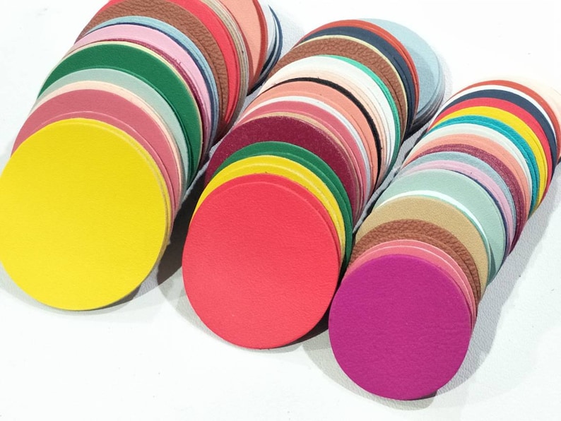 May include: A collection of colorful, circular leather pieces in various shades, including yellow, red, green, and pink. The leather circles are stacked, showcasing a variety of textures and hues. These leather pieces are suitable for crafting projects.