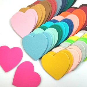 Peut inclure: Une collection de formes de cœur en feutre de différentes couleurs, dans des nuances de rose, bleu, vert, jaune, orange et rouge. Les cœurs sont disposés en demi-cercle, le plus grand cœur en haut et les plus petits cœurs en bas.