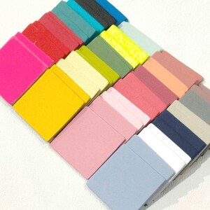 May include: A collection of 20 small, square fabric swatches in various colors, including pink, yellow, blue, green, and gray. The swatches are arranged in a staggered pattern, with the brightest colors at the top and the darker colors at the bottom.
