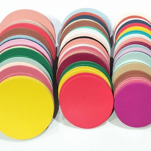 May include: A collection of colorful, round leather pieces in various shades, including yellow, red, pink, green, and brown. The leather circles are stacked in three separate piles, showcasing a range of hues and textures.