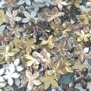 May include: A collection of metallic flower-shaped embellishments in various colors, including silver, gold, bronze, and copper. The floral shapes are scattered across a light blue surface, creating a textured appearance.