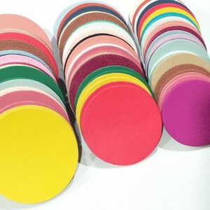 May include: A collection of colorful, circular leather pieces in various shades, including yellow, red, pink, green, and brown. The leather circles are stacked in neat piles, showcasing different textures and hues.