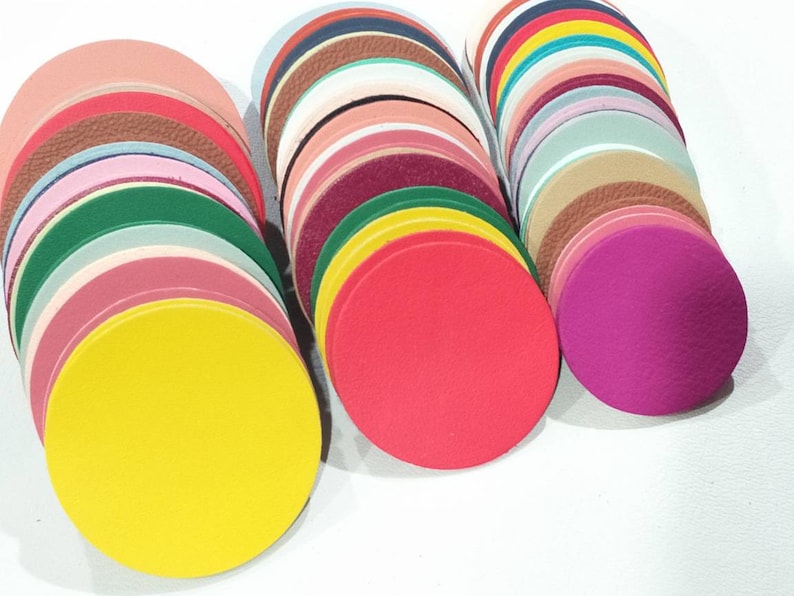May include: A collection of colorful, circular leather pieces in various shades, including yellow, red, pink, green, and brown. The leather circles are stacked in neat piles, showcasing different textures and hues.