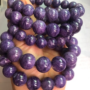 Puede incluir: Un conjunto de cuatro pulseras de piedras preciosas púrpuras con cuentas redondas. Las cuentas tienen un patrón de remolino y mármol.
