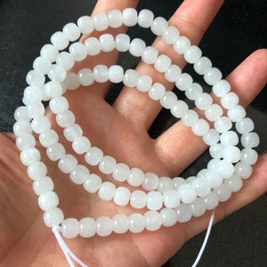 May include: A strand of white jade beads, with a smooth, rounded shape. The beads are strung on a white cord and are approximately 10mm in diameter.