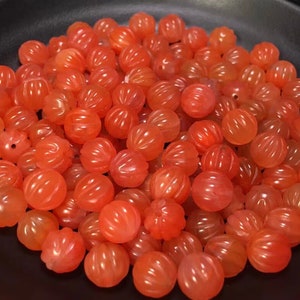 Op de afbeelding: Een verzameling feloranje, ronde kralen met een gegraveerd, getextureerd oppervlak. De kralen zijn gemaakt van agaat en zijn perfect voor het maken van sieraden.