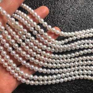 May include: Strands of lustrous, white pearls. The pearls are round and uniform in size, strung together to create multiple necklaces. The image shows a close-up view of the pearls, highlighting their smooth surface and subtle sheen. The pearls are held in a hand.