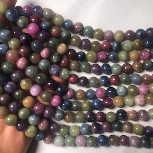 Pode incluir: Um fio de contas redondas de pedras preciosas multicoloridas. As contas são uma mistura de azuis, verdes, rosas e amarelos. As contas são todas aproximadamente do mesmo tamanho e são enfiadas em um fio transparente.