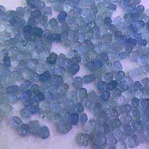 May include: A large collection of light blue aquamarine gemstones, each carved into a unique design. The stones are smooth and polished, with a translucent appearance.