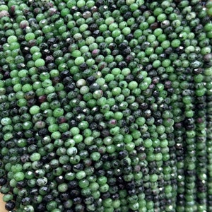 May include: A strand of green, black, and red faceted gemstone beads. The beads are round and have a smooth, polished finish.
