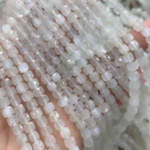 May include: A strand of white moonstone beads, each bead is faceted and has a square shape.