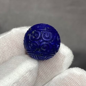 May include: A deep blue, carved lapis lazuli bead with a swirling pattern. The bead is round and has a smooth, polished surface.