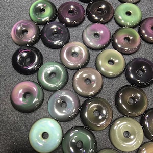 May include: A collection of iridescent, round, donut-shaped stones with a hole in the center. The stones have a variety of colors, including green, purple, and black.