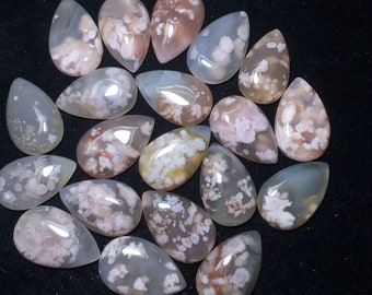 May include: A collection of 18 teardrop-shaped agate cabochons with white and pink patterns. The cabochons are polished and have a smooth, glossy finish.