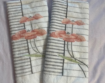 May include: Two white hand towels with a black and white striped pattern and pink floral designs. The towels have a green leaf design and a white fringe border.