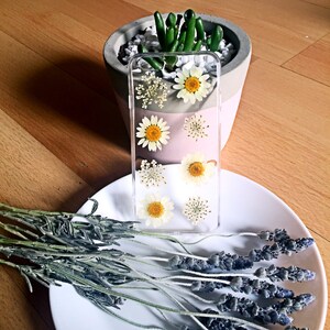 May include: A clear phone case with pressed white and yellow flowers. The case is on a white plate with dried lavender sprigs.