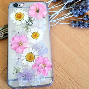 May include: A clear phone case with pressed flowers. The case features pink, white, and purple flowers.