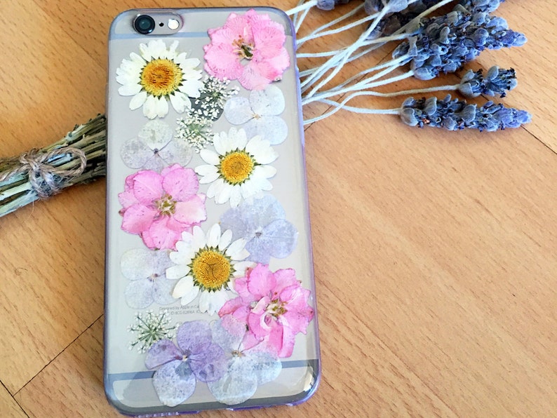 May include: A clear phone case with pressed flowers. The case features pink, white, and purple flowers.