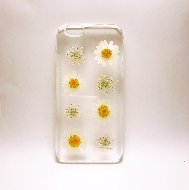 May include: A clear phone case with pressed white flowers and yellow centres. The flowers are arranged in a grid pattern.