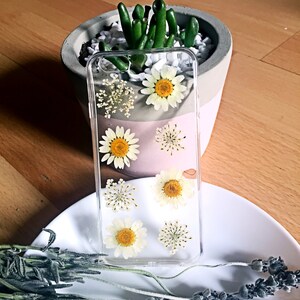 May include: A clear phone case with pressed white flowers and yellow centres. The flowers are arranged in a symmetrical pattern.